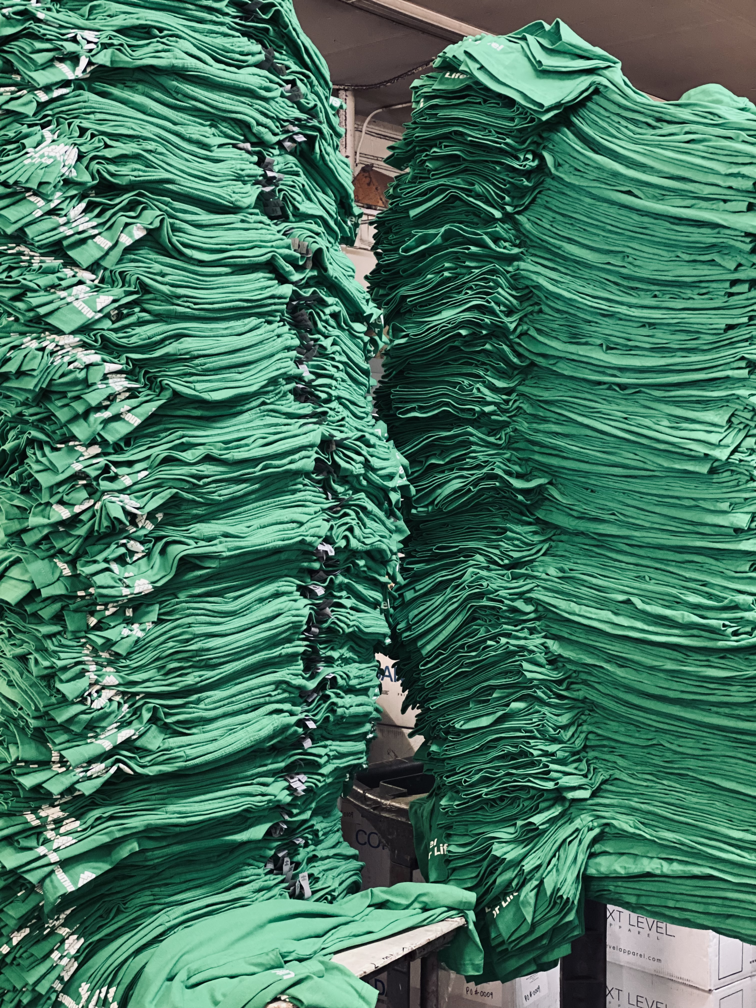 Towering stacks of bulk green t-shirts ready for printing
